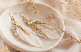 Ivory and gold feather earrings arranged on a ceramic dish